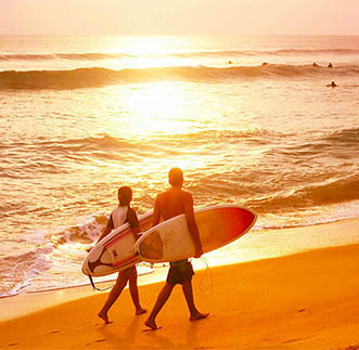 Couple of surfers walks along the beach in Hikkaduwa